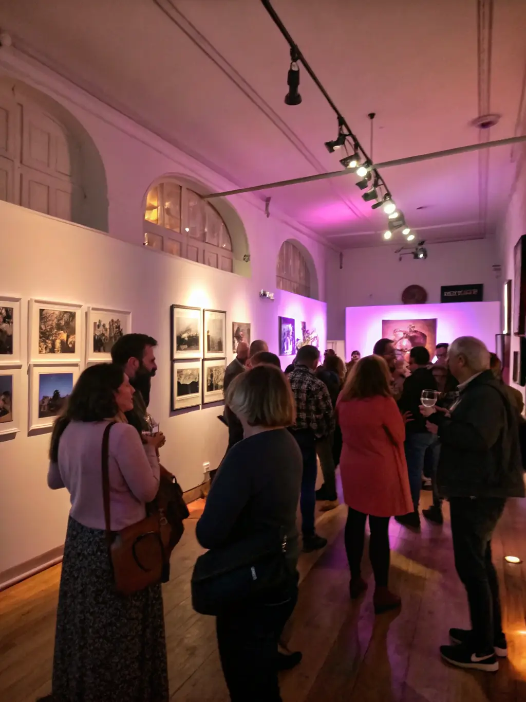 A photograph of an art exhibition opening night, featuring artists, curators, and attendees admiring the displayed artworks, highlighting LE COIN DU MIROIR's role in promoting contemporary art.